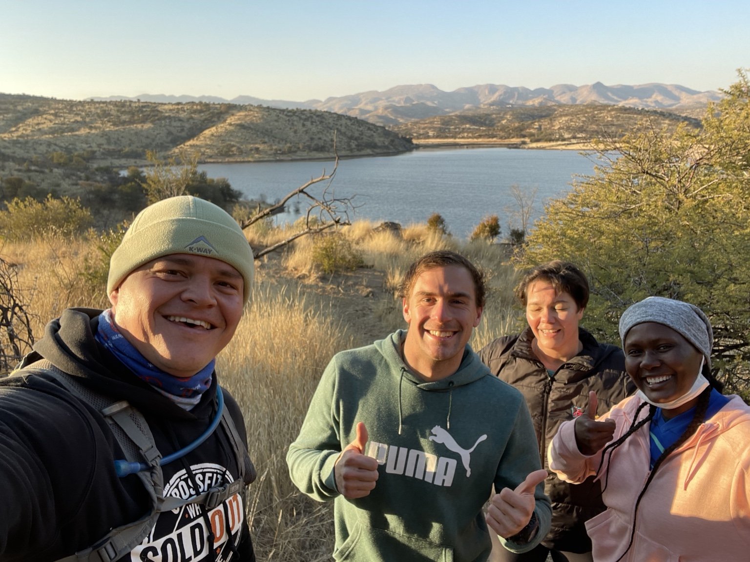A group smiling together beside a dam and mountains